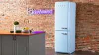 A tall blue Smeg column refrigerator stands in front of a brick wall