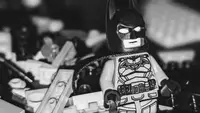 Close-up of a Batman Lego mini figure with a pile of gray and black Lego bricks in the background.