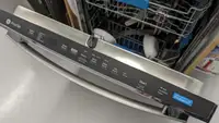 A stainless steel dishwasher door stands open and shows its top-facing control panel