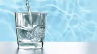 Tap water being poured into a short glass with water in background.