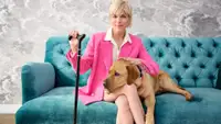 Selma Blair, QVC Brand Ambassador For Accessibility, Sits On A Plush Teal Sofa With Her Dog, Scout. She Wears A Hot Pink Suit And Uses A Black And Gold Cane.