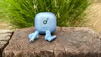 The Anker Soundcore Liberty 4 NC earbuds and case in light blue sitting on a wooden wall with a plant in the background.