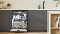 Open Bosch dishwasher, revealing three racks full of dishware, in a modern kitchen