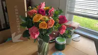 A bright bouquet of flowers from UrbanStems sitting on a wood table by a window