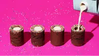 Milk being poured into cylindrical desserts on a neon pink background