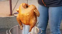 Fried turkey hanging above a pot outdoors