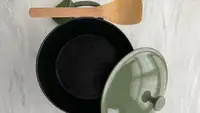 Our Place Cast Iron Perfect Pot in sage green color with lid removed next to wooden spoon.