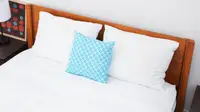 A bed with white sheets and a blue pillow