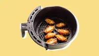 A batch of chicken wings in an air fryer basket, on a yellow background