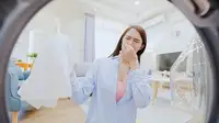 A woman noticing a bad smell coming from her washing machine.