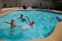 Three youths play pool basketball in an in-ground swimming pool.