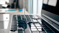 A stream of water spills on a laptop keyboard