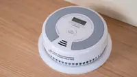 A round, white smoke detector sits on a wood background