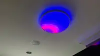 Smart ceiling fixture illuminating a room with vivid blue and magenta lighting, demonstrating customizable RGB ambient effects and ceiling wash lighting.