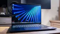Dell 14S (DS14260) laptop open and turned on, sitting on a wooden surface. Blue abstract image displayed on screen.