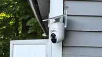 White Elysoo 4K Wifi Solar Camera mounted on a grey house with trees in the background.