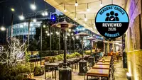 A string-lit outdoor patio dining area with tables, chairs, and patio heaters, with a 
