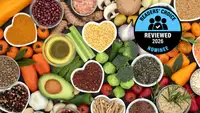 An overhead view of fresh vegetables, legumes, and spices arranged on a dark surface, with a 