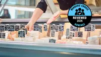 A deli case with an assortment of labeled cheeses, with a 