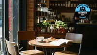 A coffee cup and croissant on a small wooden café table next to an open book.