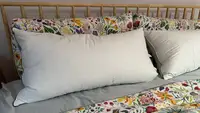 Two white Pacific Coast Feather & Down Pillows on a bed with floral sheets and a wooden barred headboard.