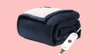 A folded blue electric blanket with a white sherpa lining is shown against a pink background.