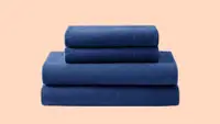 Navy blue folded sheet set against a peach-colored background.