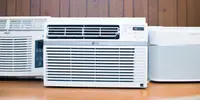 Three of the best window air conditioners are displayed on a wooden countertop, all are white.