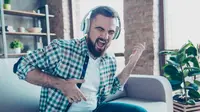 A man listening to headphones while playing the air guitar.