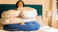 Writer Steph Garcia sits on a bed surrounding by pregnancy pillows.