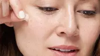 A woman taking a pimple patch off of her face.
