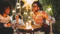 A family laughs around an outdoor fireplace