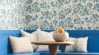 Blue wooden seating in the corner with white pillows and a blue floral decorative wallpaper from Rifle Paper Co.