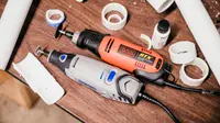 Black and decker rotary tool and a dremel sit side by side on a work bench surrounded by cut pipes
