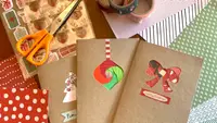 Homemade Christmas cards laying on top of decorative paper, stickers, washi tape, scissors