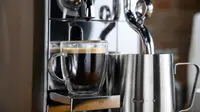 A close-up photo of the Breville Nespresso Creatista brewing an espresso shot and frothing milk.