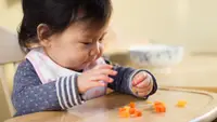 baby girl sitting in a high chair eating food with her hands