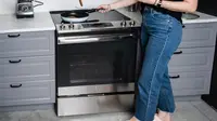 A person wearing jeans stands in front of an electric range cooking food in a pan on the stovetop.