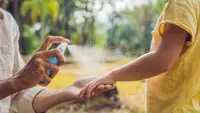 Person spraying mosquito repellent on child's arm while outdoors