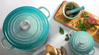 A teal Le Creuset dutch oven sitting on a countertop next to a charcuterie board.