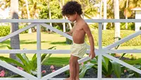Little boy wearing swim trunks and standing on a railing