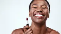 Woman smiling while holding a tube of brown nude lipstick