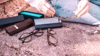 Two pairs of glasses and their boxes are spread out on a sidewalk while a woman holds a third pair.