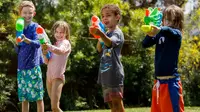 Four kids lined up outside shooting water guns and Nerf Super Soakers