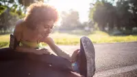 A woman wearing workout gear stretching on pavement outside.