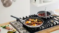 A brightly lit kitchen featuring a gas cooktop with two frying pans filled with food.