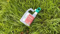 A bottle of organic liquid lawn care treatment sits on a bed of lush green grass.