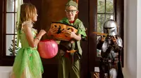 Three kids wearing Halloween costumes: Tinker Bell, Peter Pan, and the Mandalorian