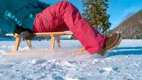 A model wearing snow pants glides across a frozen lake on a sled.