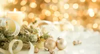 Gold Christmas ornaments surround white burning candle and Christmas lights.